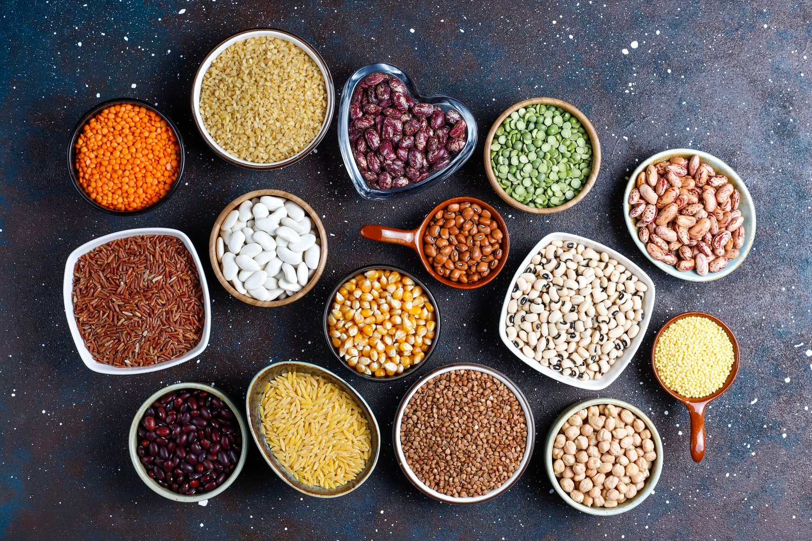 Legumes and beans assortment in different bowls on light stone b